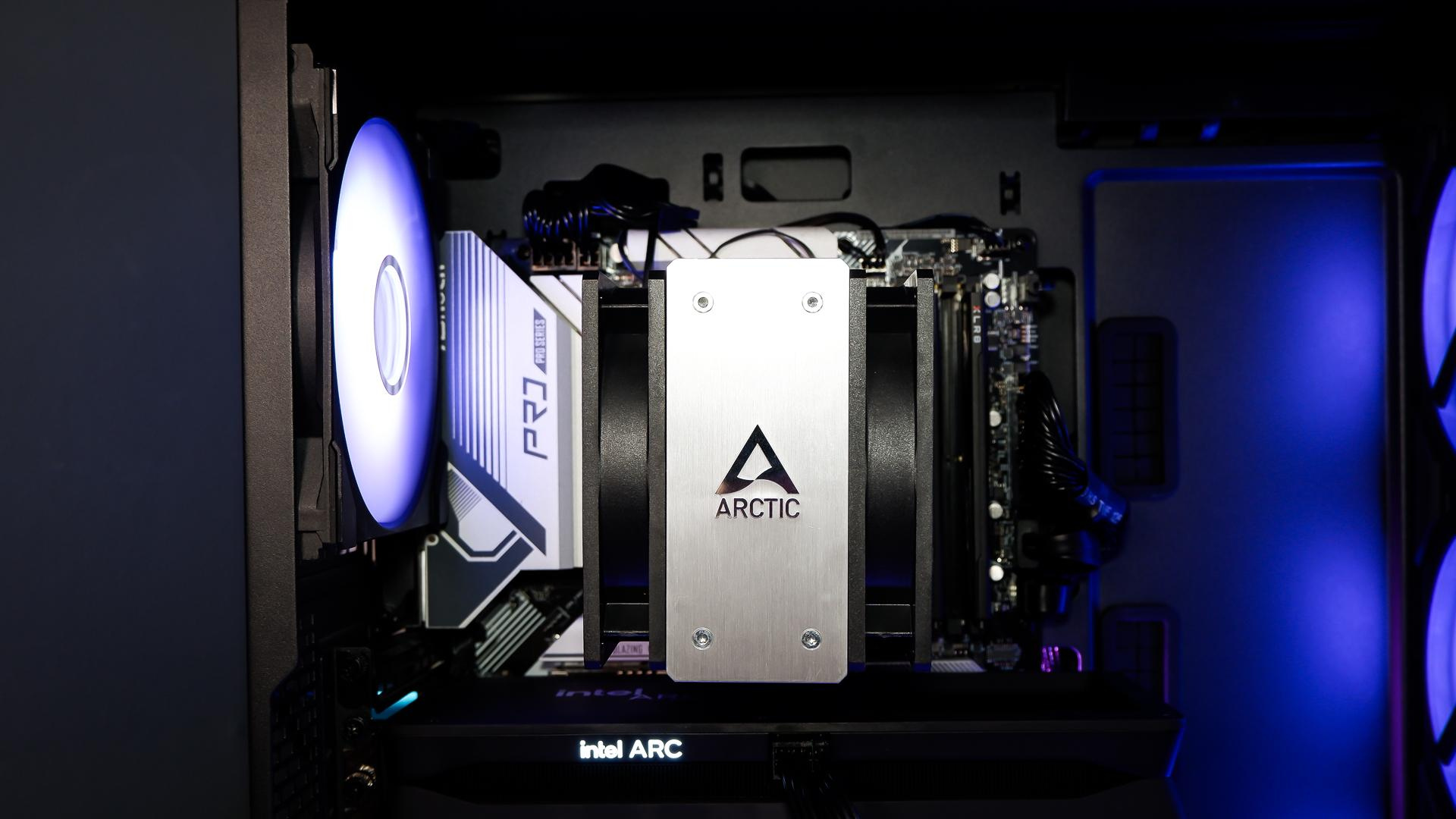 A gaming PC sat on a desk with purple RGB lighting on the fans and light bar enabled.